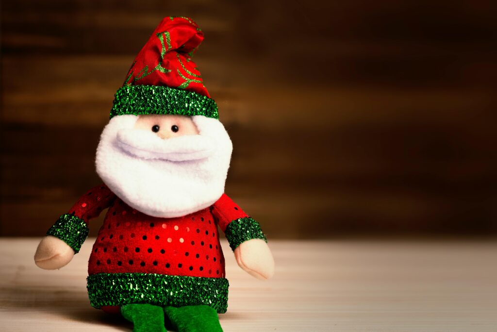 A toy Santa sits on a platform in front of a dark wooden wall